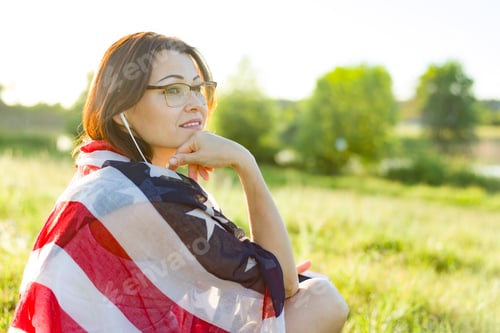 Preview: Mature woman listens to music, an audiobook on headphones, relaxes in nature.