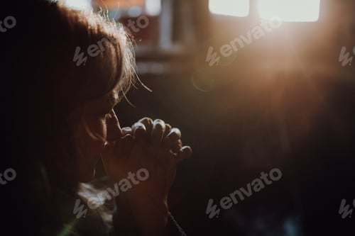 Preview: Close-up of unhappy elderly woman praying, black background.