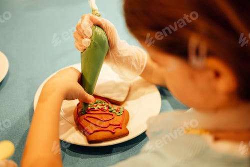 Preview: Close-up of a girl painting Christmas cookies with a pastry bag.