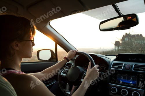 Preview: Close up view of a woman driver holding steering wheel driving a car at sunset.