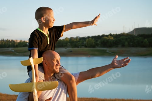 Preview: Father holding son on shoulders at sunset with airplane in hand