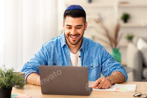 Preview: Smiling israeli man working on laptop at home
