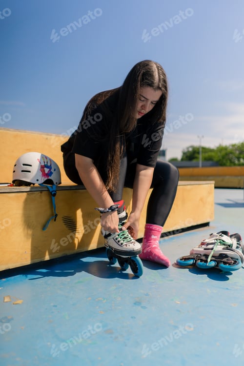 Preview: hipster girl wearing roller skates tying laces in skate park before skating street extreme sport