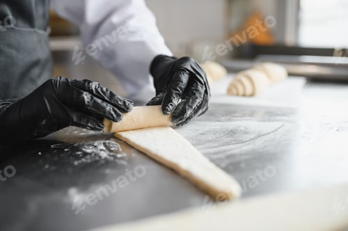 Preview: Baker rolling dough for croissants in bakery kitchen
