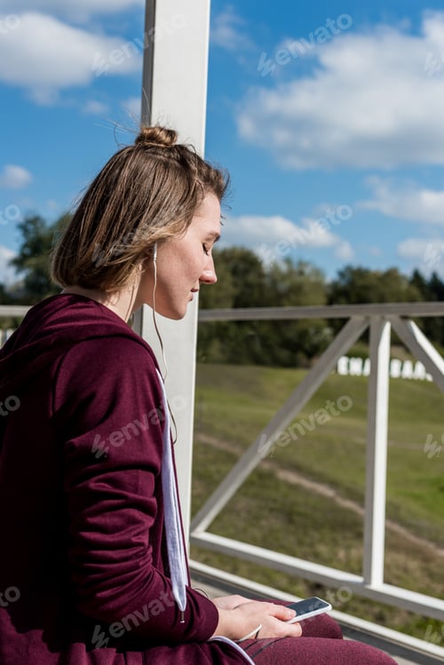 Preview: young thoughtful woman listening music with earphones outdoors