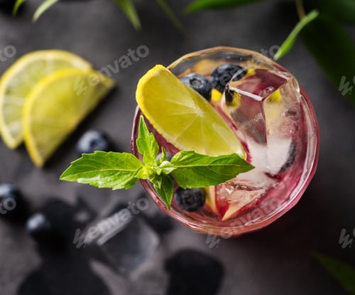 Vista previa: Mojito de arándanos o limonada con lima, hielo y menta en un vaso sobre fondo oscuro