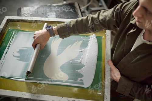 Preview: Young Man Screen Printing Graphic Design Onto Surface in Workshop