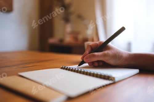 Preview: Closeup image of a hand holding a pen and writing on notebook on wooden table