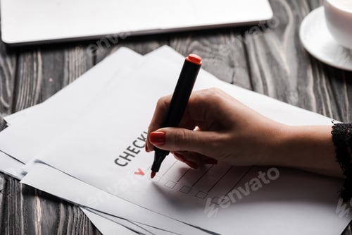 Preview: cropped view of woman holding marker pen near checklist on table