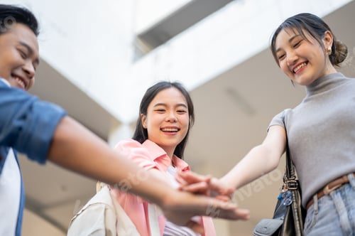 Preview: Asian woman student and a man friend joining hands together while standing below university building
