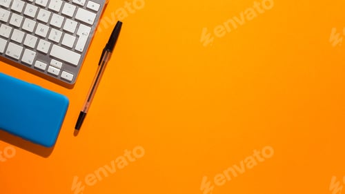 Preview: Top view of a smartphone and a keyboard with a pen on an orange background