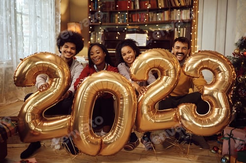 Visualização: Amigos felizes segurando balões enquanto comemoram o Ano Novo de 2023 em casa e olhando para a câmera.