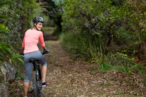 Preview: Woman riding mountain bicycle on narrow dirt trail through dense forest, wearing helmet and gloves