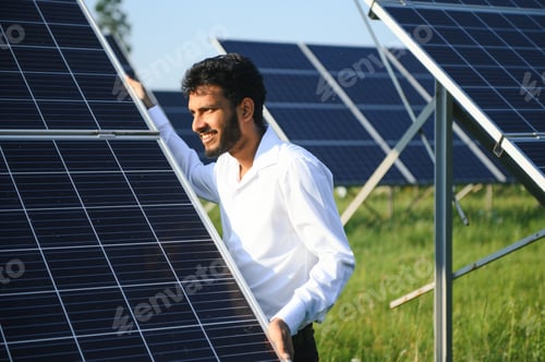 Preview: An Indian male engineer in a green vest is working on a field of solar panels.