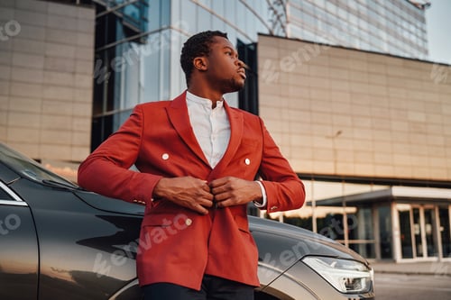 Preview: Cool african businessman posing against building with his car