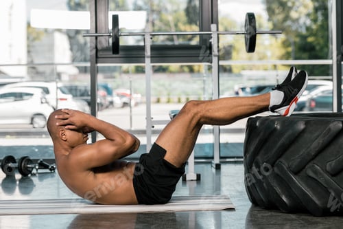 Preview: side view of african american man doing abs on fitness mat at gym