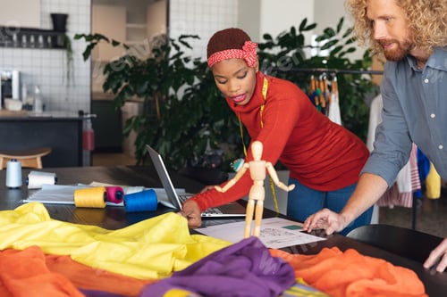 Preview: Multiracial male and female fashion designers discussing over sketch at desk in studio office