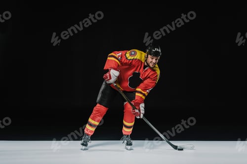 Preview: full length view of young professional sportsman playing ice hockey on black