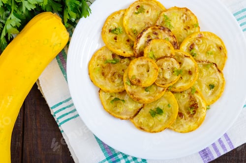 Preview: Fried zucchini slices on a white plate on a dark wooden background. Top view.