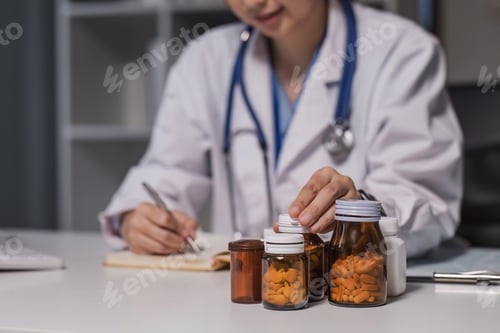 Visualização: Médica asiática, médica, terapeuta de clínica geral, usa jaleco branco segurando o frasco de comprimidos à mão, escrevendo para fins médicos