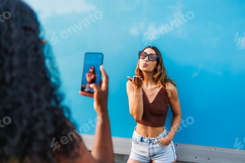 Preview: Woman posing with a kiss gesture while friend records video on a smartphone
