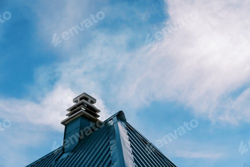 Preview: Smoke rises from a chimney on the green corrugated roof of a house against the blue sky