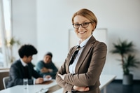 Preview: Portrait of happy mature CEO standing with her with arms crossed in office and looking at camera.