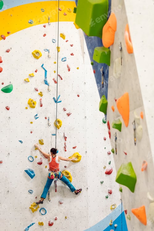 Preview: Young Woman rock climbing indoors.