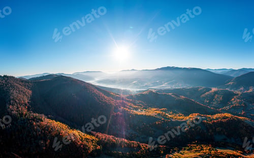 Preview: High mountain peaks with yellowed forest under bright sun