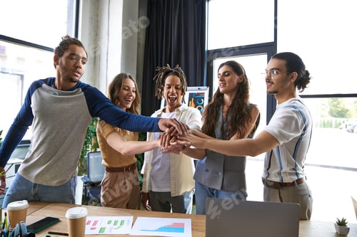 Preview: joyful multicultural business people joining hands near graphs and laptop in office, unity gesture