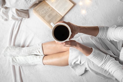 Vorschau: Tasse Kaffee in Frauenhänden im Bett, Ansicht von oben.