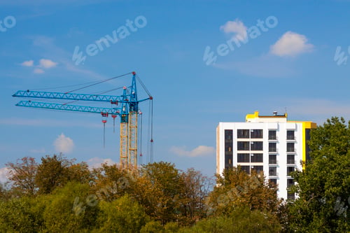 Preview: Tower cranes on a construction site near building and green trees