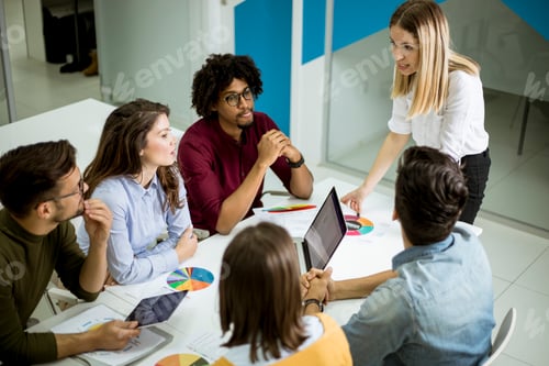 Preview: Pretty female team leader talking with mixed race group of people in the office