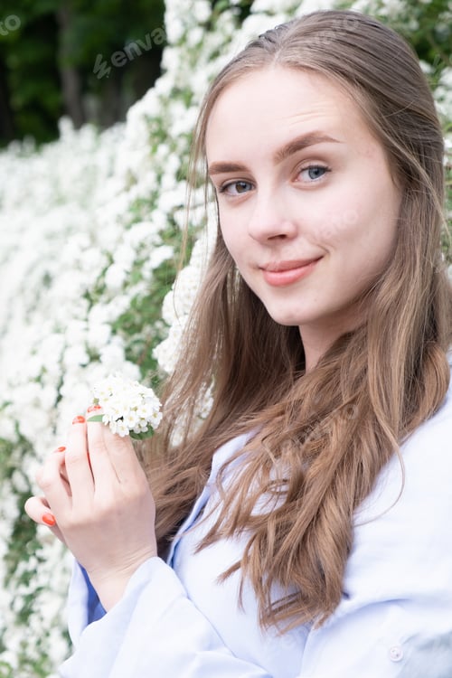 Preview: beautiful young girl in a city park near flowering spirea bushes