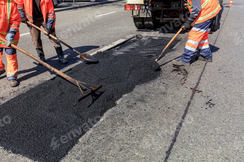Preview: The working team evenly distributes part of the asphalt with shovels during road construction.