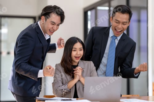 Preview: Business team celebrating success at the office with raised fists.