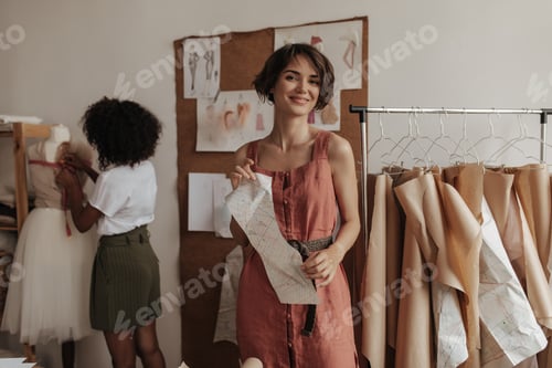 Preview: Cheerful young girls in trendy outfits work as fashion designers. Short-haired woman in linen dress