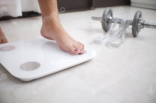 Preview: Cropped image of woman feet standing on weigh scales, A tape measure and dumbbell in the foreground