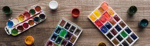 Preview: top view of colorful paint palettes on wooden brown table with gouache, panoramic shot