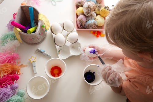 Preview: Children's hands paint Easter eggs with elements of spring decor table top view