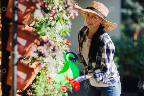 Preview: Beautiful female gardener watering plants in the garden in hot summer day. Gardening concept