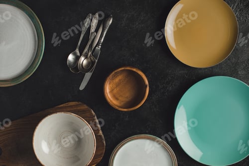 Preview: flat lay with arranged ceramic plates, antique silverware and cutting board isolated on black
