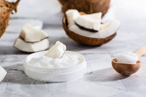 Preview: A piece of coconut in coconut oil in a jar and a wooden spoon with oil and coconut on the table.