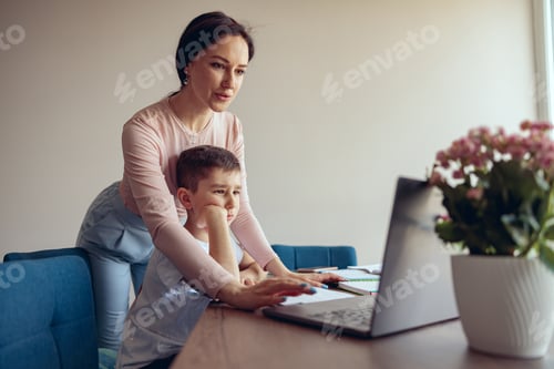 Preview: Beautiful young mother helping little son schoolboy in online learning at laptop.