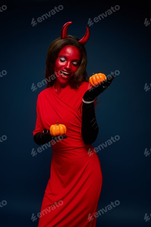 Preview: A striking woman embraces Halloween with a devil costume and vibrant pumpkin in a stylish setting