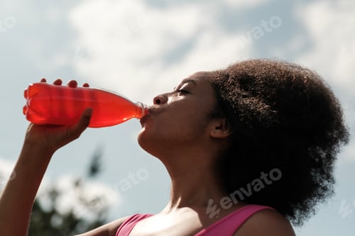 Preview: Young sporty woman drinking refreshing soda from bottle in summer