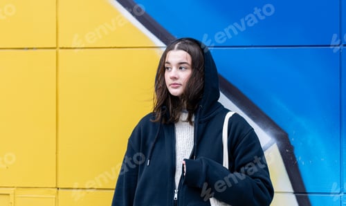 Preview: A young woman against a yellow-blue wall, urban graffiti.