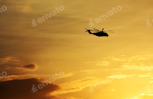 Preview: Helicopter’s silhouette on the golden sky of an amazing sunset background with copy space.