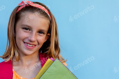 Preview: Happy caucasian schoolgirl with school bag and books over blue background at elementary school