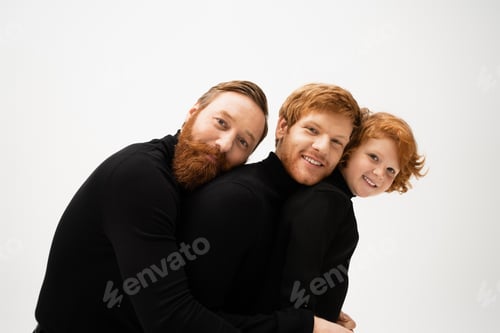 Preview: cheerful redhead men and kid in black sweaters leaning on each other and smiling at camera isolated